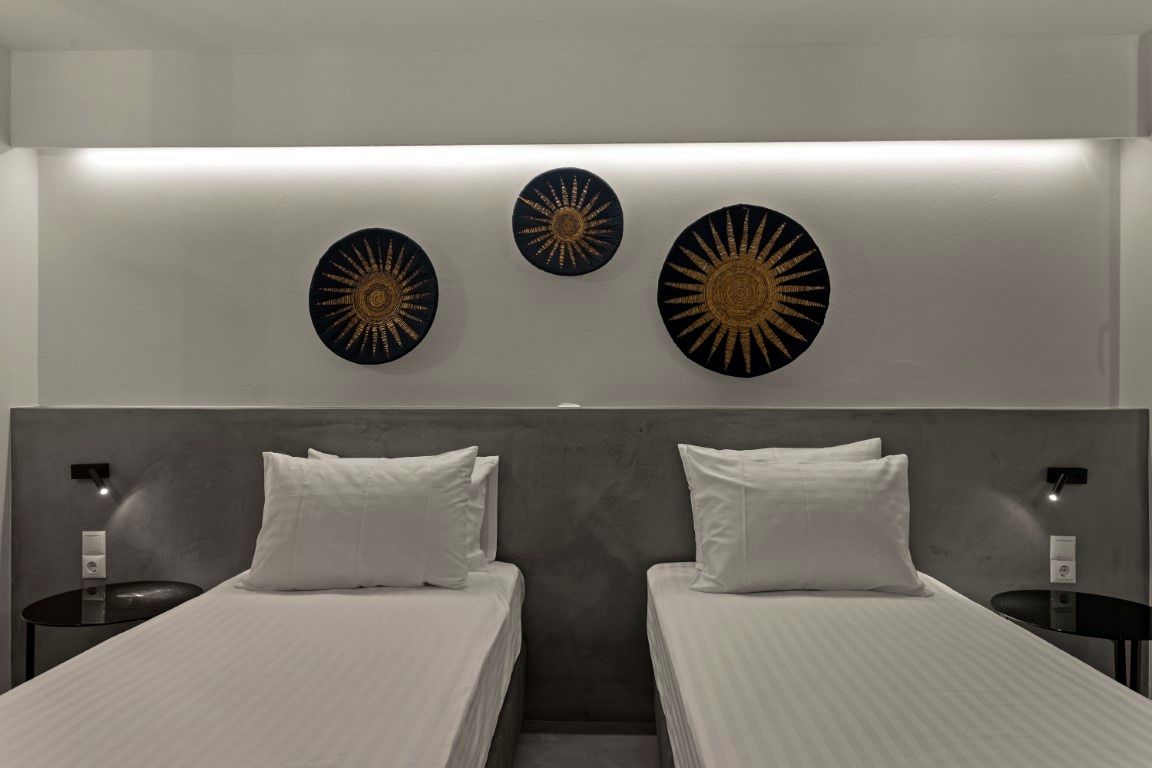 Two twin beds with white linens are positioned below a wall displaying three circular, radiating gold and black decorations.