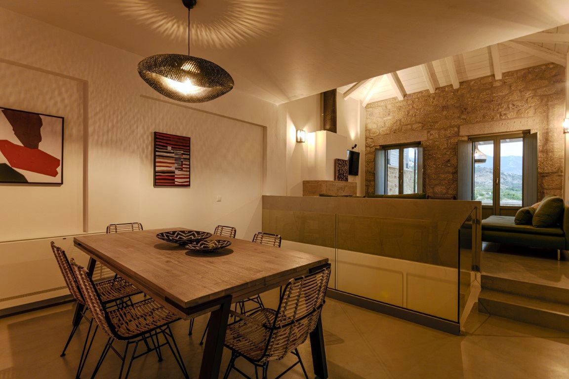 Large wooden dining table with dark chairs sits in a room with exposed brick walls and two glass doors leading outside.