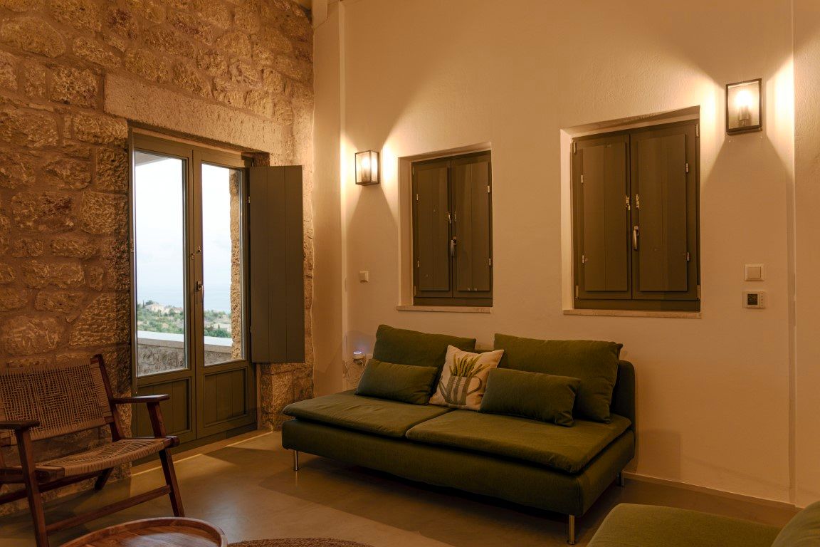 A green sofa sits against a light-colored wall featuring two paneled closets. To the left, a doorway with glass panels opens onto an exterior view. A woven chair rests near the doorway.