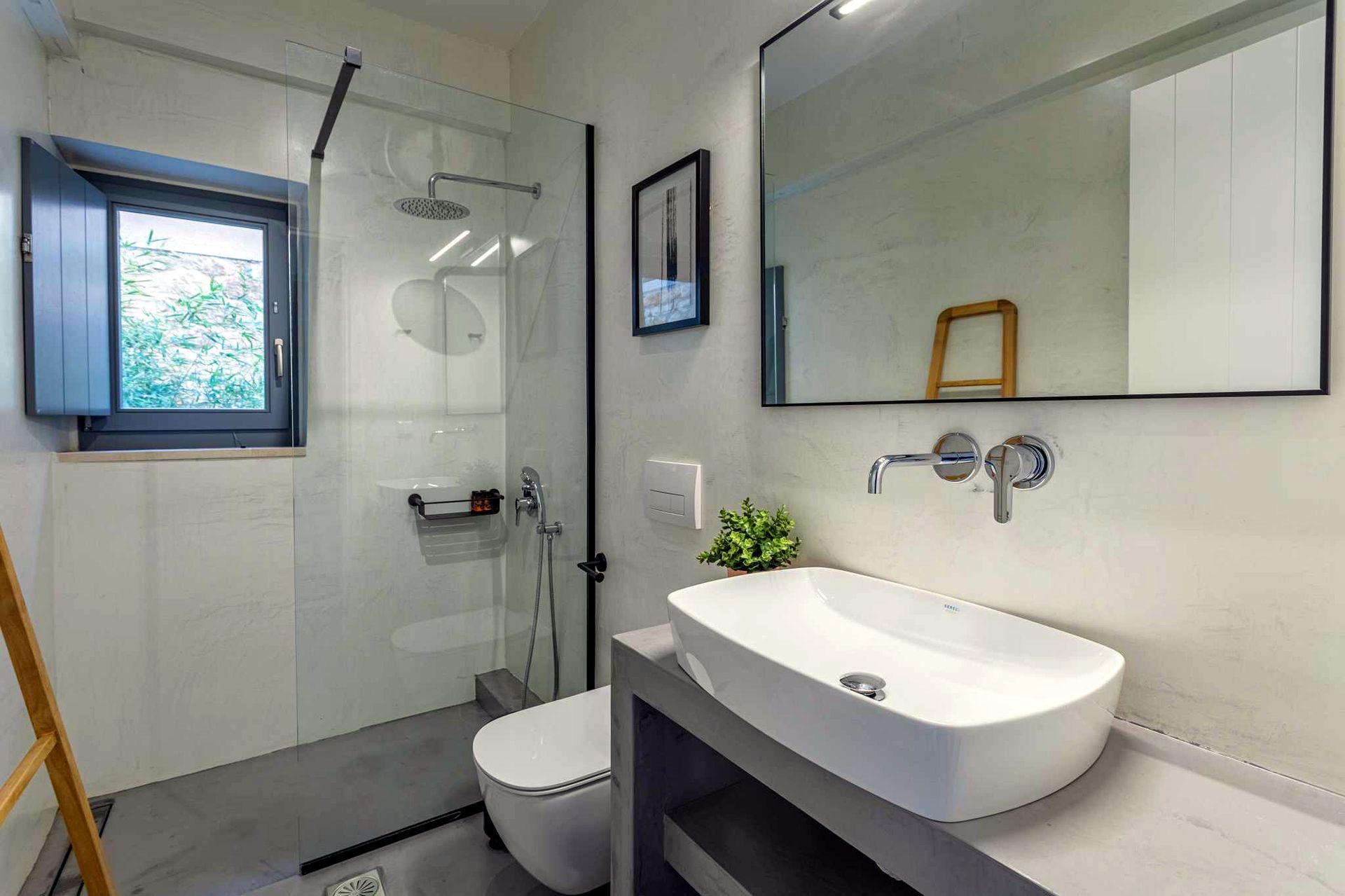White rectangular basin sits on a gray countertop beneath a large rectangular mirror. To the left, a glass enclosure separates a shower area with a visible window.