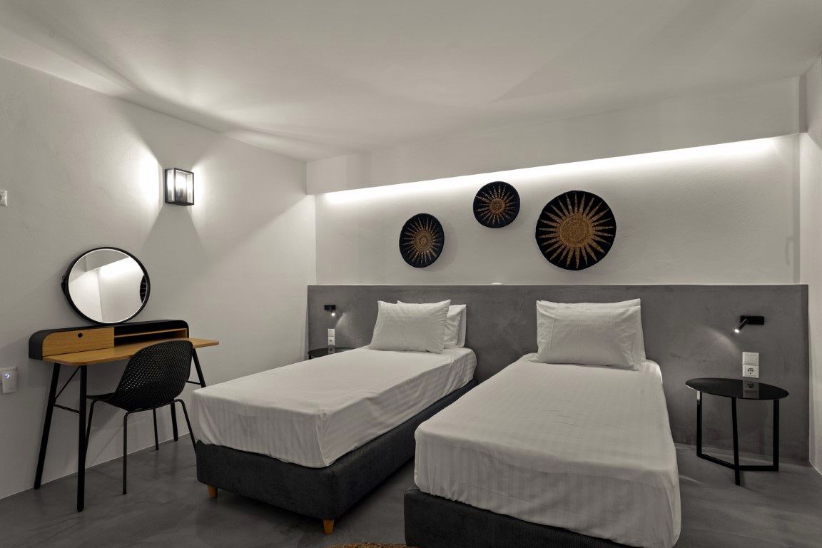 Two twin beds with white linens are positioned against a gray wall featuring three circular, dark patterned wall hangings. A wooden desk with a round mirror is visible on the left.